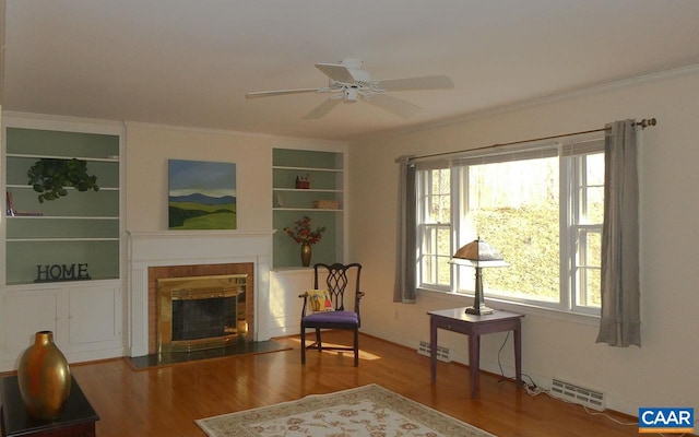 living area featuring built in shelves, ornamental molding, a healthy amount of sunlight, and hardwood / wood-style flooring