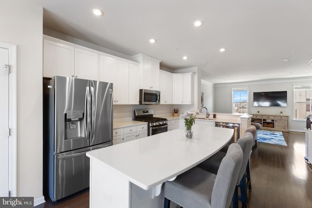 kitchen featuring a breakfast bar, a center island, kitchen peninsula, stainless steel appliances, and white cabinets