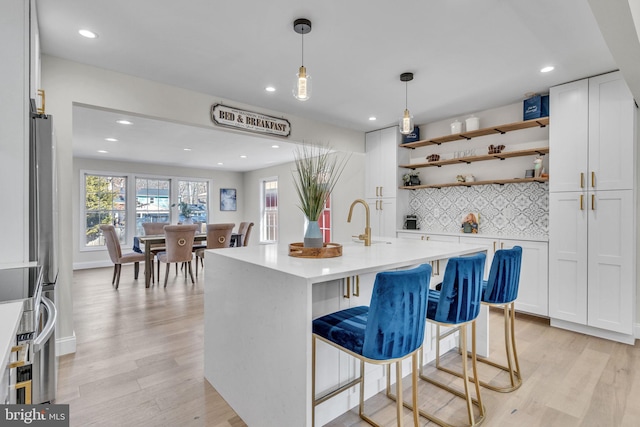 kitchen featuring open shelves, light countertops, a kitchen island with sink, white cabinets, and light wood-type flooring