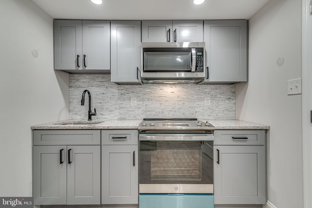 kitchen with appliances with stainless steel finishes, a sink, light stone counters, and gray cabinetry