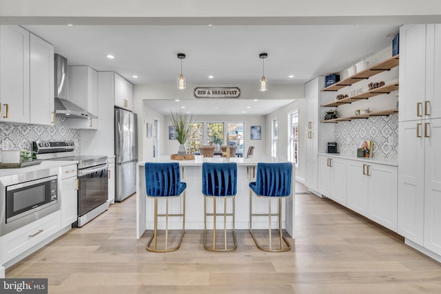 kitchen featuring white cabinetry, light countertops, wall chimney range hood, appliances with stainless steel finishes, and open shelves