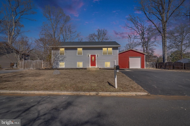 bi-level home with entry steps, an outdoor structure, fence, a detached garage, and driveway