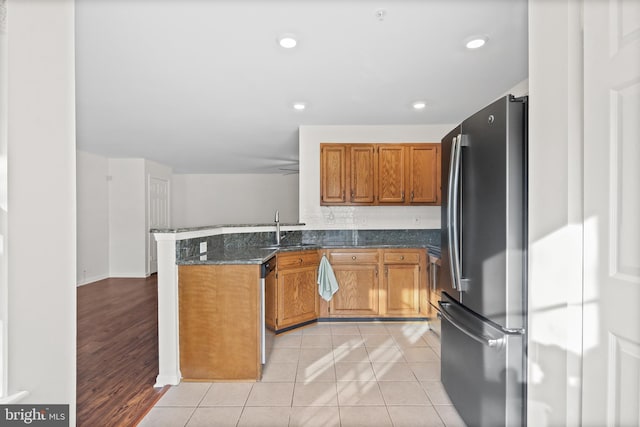 kitchen featuring sink, light tile patterned floors, dark stone counters, kitchen peninsula, and stainless steel appliances