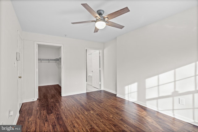 unfurnished bedroom with dark wood-type flooring, ceiling fan, ensuite bathroom, a spacious closet, and a closet