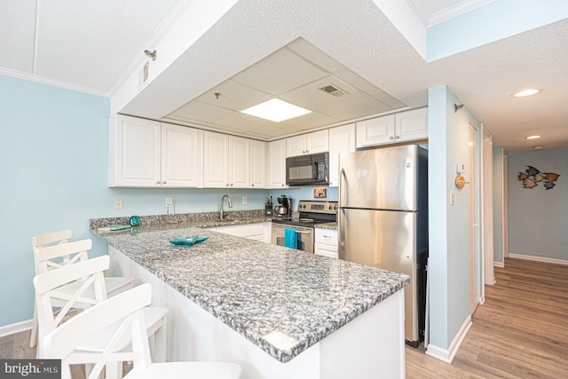 kitchen featuring appliances with stainless steel finishes, a breakfast bar, white cabinets, kitchen peninsula, and light stone countertops