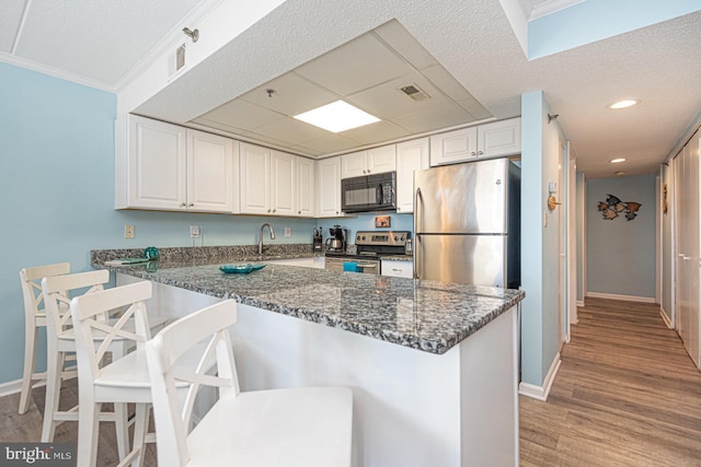 kitchen featuring white cabinetry, kitchen peninsula, dark stone countertops, and appliances with stainless steel finishes