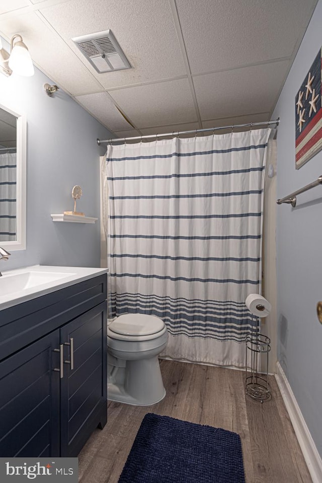 bathroom with toilet, a shower with curtain, a paneled ceiling, vanity, and hardwood / wood-style floors