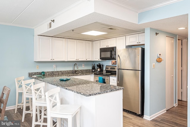 kitchen with white cabinetry, appliances with stainless steel finishes, dark stone counters, and kitchen peninsula