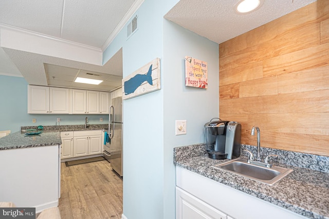 kitchen featuring wood walls, white cabinetry, sink, ornamental molding, and light wood-type flooring