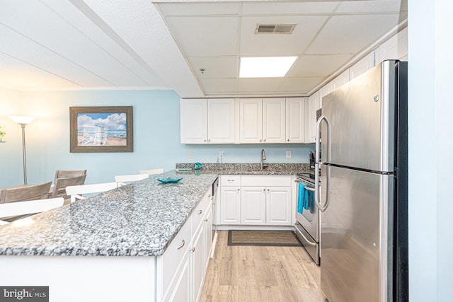 kitchen featuring light hardwood / wood-style flooring, a paneled ceiling, appliances with stainless steel finishes, light stone countertops, and white cabinets