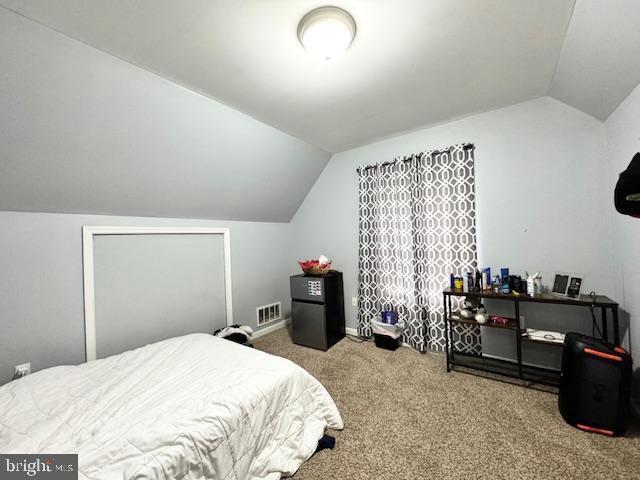 bedroom with black refrigerator, lofted ceiling, and carpet floors