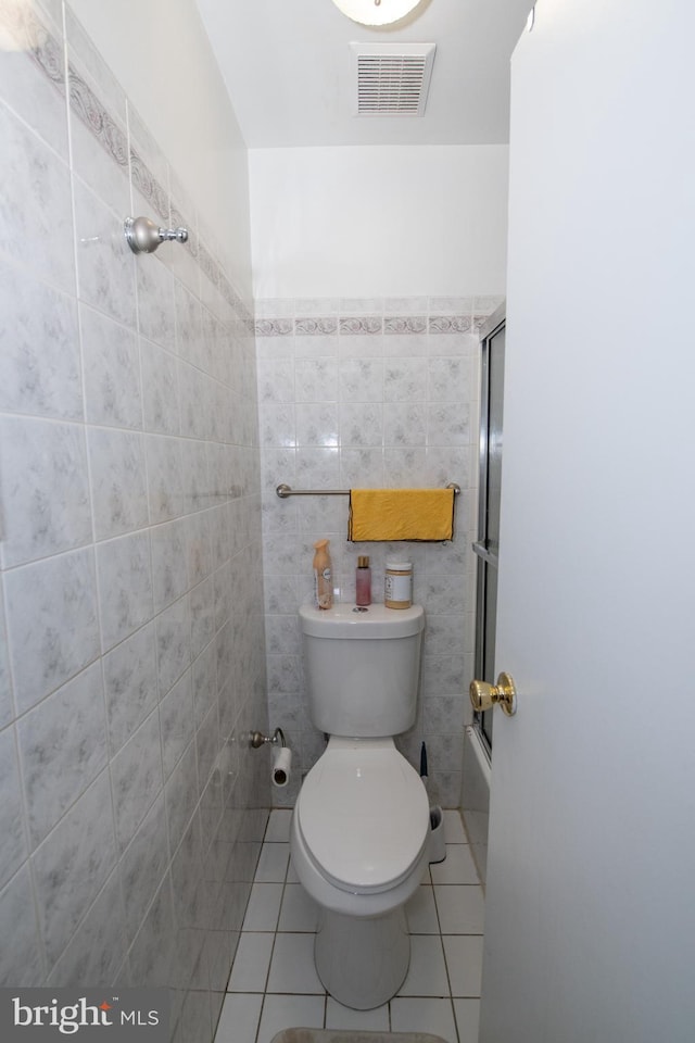 bathroom with tile walls, tile patterned flooring, shower / bath combination with glass door, and toilet