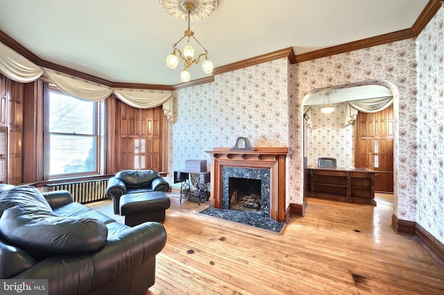 living room featuring radiator, a high end fireplace, an inviting chandelier, wood-type flooring, and crown molding