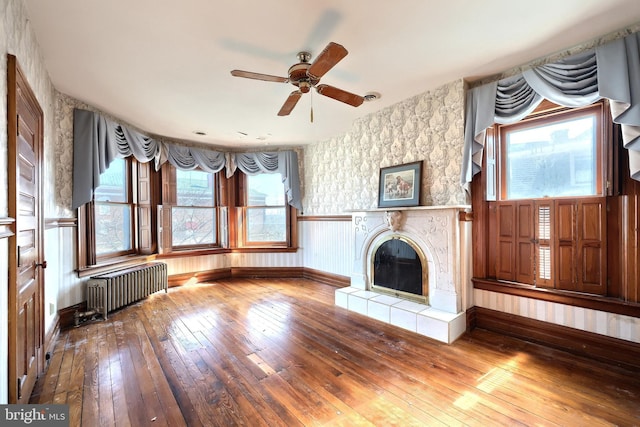 unfurnished living room featuring radiator, ceiling fan, wood-type flooring, and a fireplace