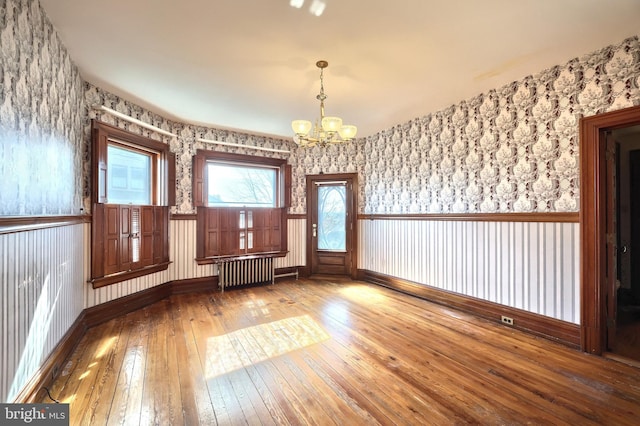 empty room with a notable chandelier, hardwood / wood-style floors, and radiator heating unit