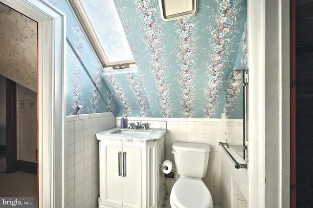 bathroom with toilet, vanity, a skylight, and tile walls