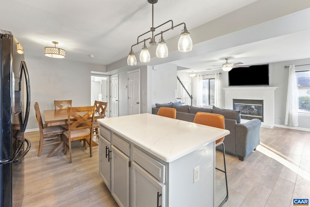 kitchen featuring black fridge with ice dispenser, hanging light fixtures, light wood-type flooring, gray cabinets, and a kitchen island