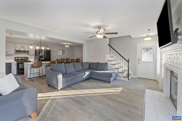 living room with a fireplace, ceiling fan, and light wood-type flooring