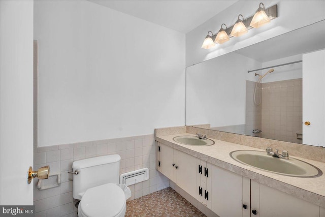 bathroom with tile walls, vanity, toilet, and tiled shower