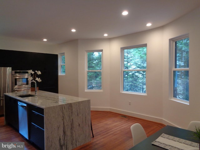 kitchen featuring dishwasher, sink, oven, a kitchen island with sink, and light stone counters