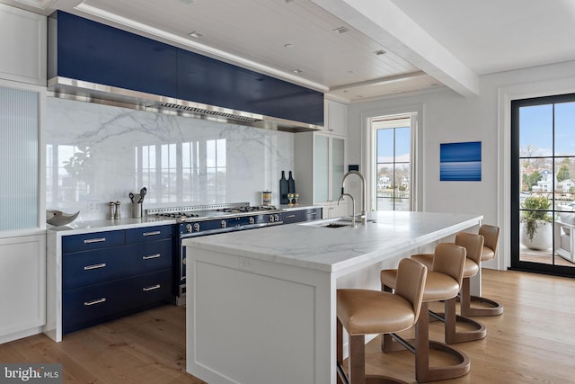 kitchen featuring a breakfast bar, sink, white cabinetry, an island with sink, and high end stainless steel range oven