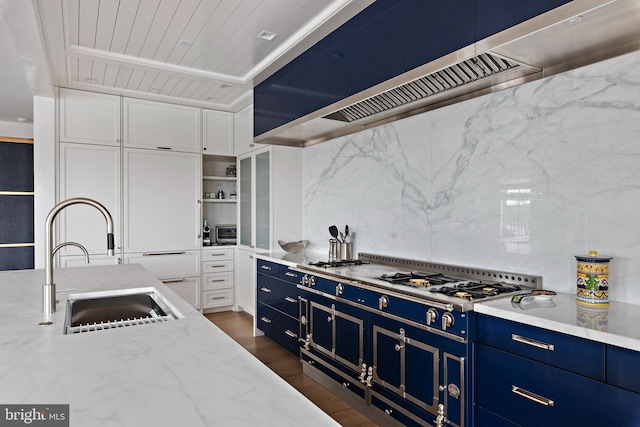 kitchen with wall chimney range hood, sink, dark wood-type flooring, light stone countertops, and white cabinets