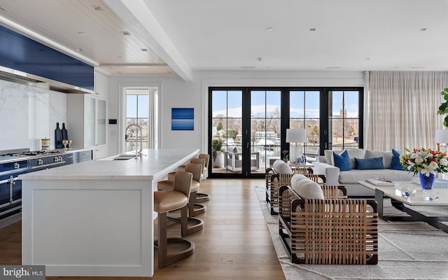 living room featuring sink, french doors, beamed ceiling, and light wood-type flooring