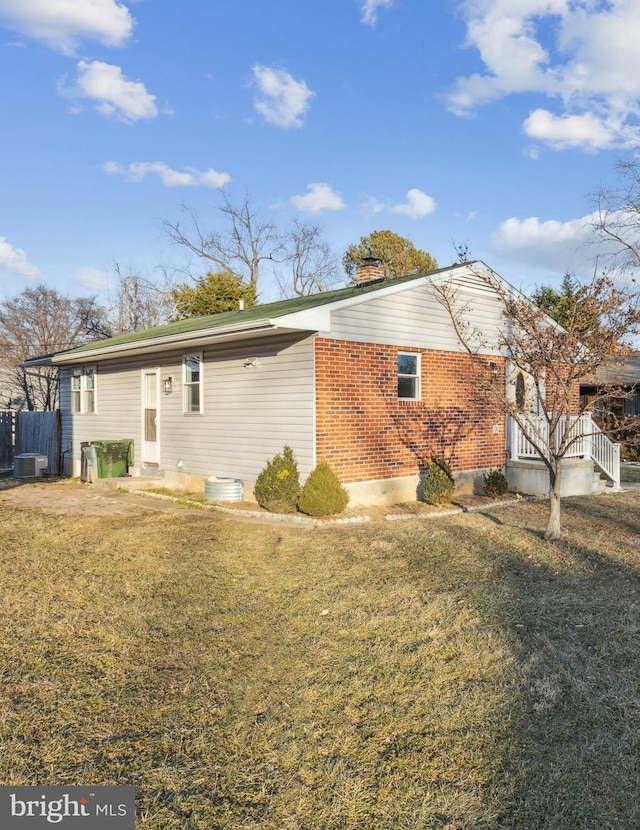 exterior space with a chimney, a front lawn, central AC, and brick siding