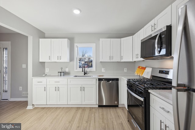 kitchen with stainless steel appliances, light countertops, a sink, and light wood finished floors