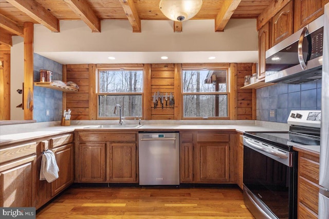 kitchen featuring sink, light hardwood / wood-style flooring, stainless steel appliances, and beamed ceiling