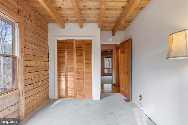 unfurnished bedroom featuring beamed ceiling, light carpet, wooden ceiling, and a closet