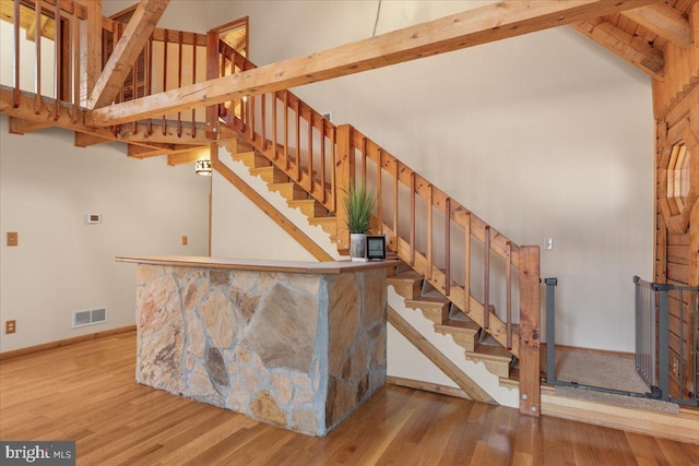 stairs featuring wood-type flooring, high vaulted ceiling, and beam ceiling