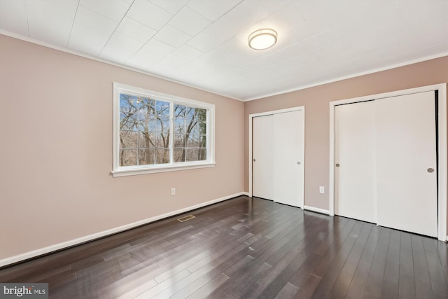 unfurnished bedroom featuring dark hardwood / wood-style flooring, crown molding, and multiple closets