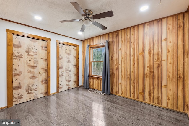 empty room with dark hardwood / wood-style flooring, wooden walls, ornamental molding, and a textured ceiling