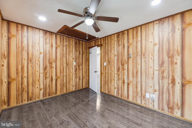 unfurnished room featuring ceiling fan, dark wood-type flooring, wooden walls, and a textured ceiling