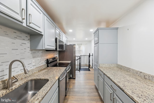 kitchen featuring tasteful backsplash, sink, stainless steel appliances, light stone countertops, and light wood-type flooring