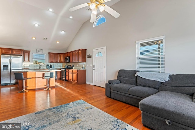 living room with ceiling fan, light wood-type flooring, sink, and high vaulted ceiling