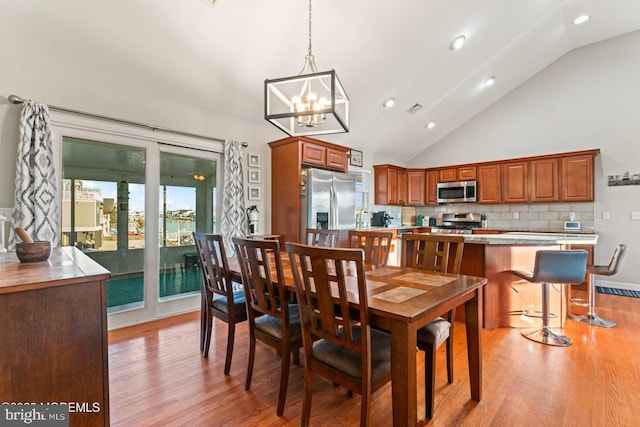 dining space featuring high vaulted ceiling, an inviting chandelier, and light wood-type flooring