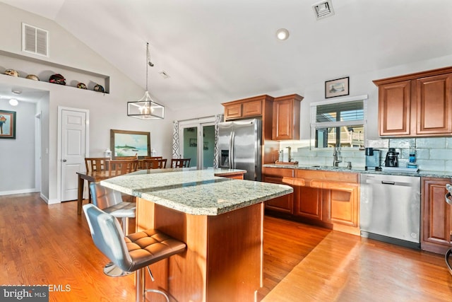 kitchen featuring appliances with stainless steel finishes, backsplash, light stone counters, a kitchen island, and decorative light fixtures