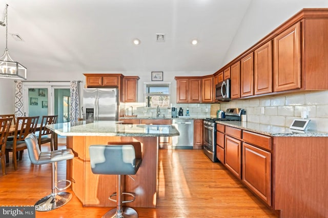 kitchen featuring tasteful backsplash, a center island, hanging light fixtures, appliances with stainless steel finishes, and light stone countertops