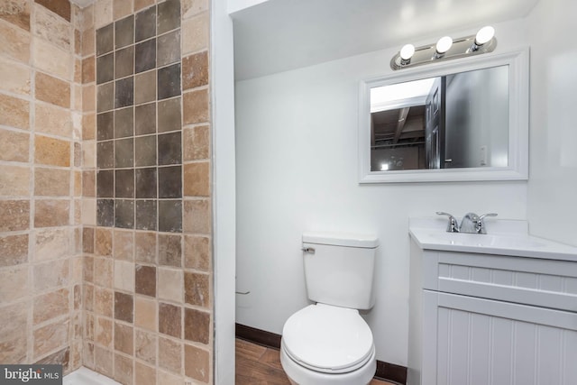 bathroom with vanity, wood-type flooring, a tile shower, and toilet