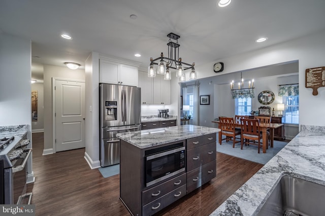 kitchen with pendant lighting, appliances with stainless steel finishes, white cabinetry, light stone countertops, and dark hardwood / wood-style flooring