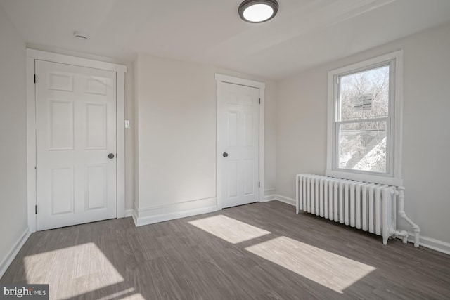 unfurnished bedroom featuring radiator heating unit and dark hardwood / wood-style flooring