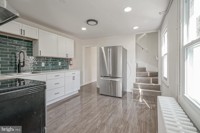 kitchen featuring sink, white cabinetry, radiator heating unit, stainless steel fridge, and decorative backsplash