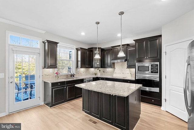 kitchen with hanging light fixtures, a kitchen island, sink, appliances with stainless steel finishes, and decorative backsplash