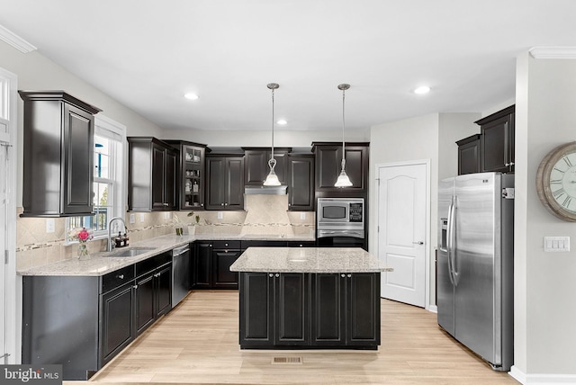 kitchen with stainless steel appliances, light stone countertops, decorative light fixtures, a center island, and sink