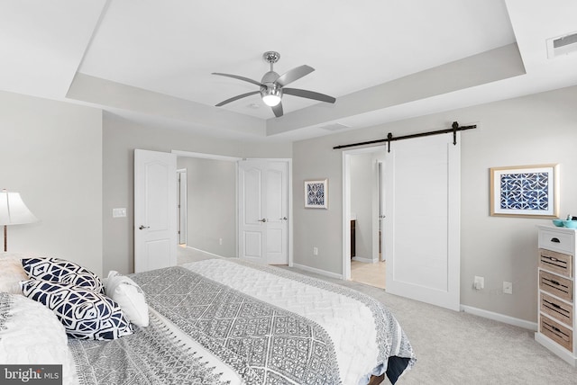 bedroom with a raised ceiling, light carpet, ceiling fan, and a barn door