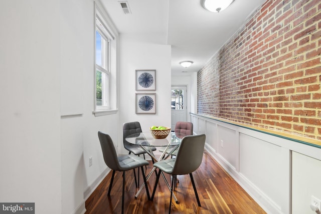 dining room featuring dark wood-type flooring and brick wall