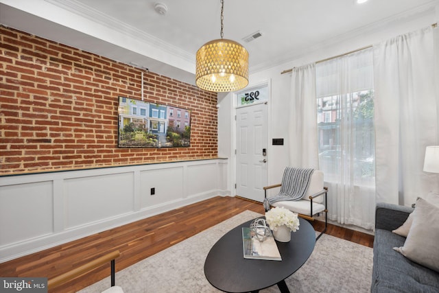 living room featuring ornamental molding, brick wall, hardwood / wood-style floors, and an inviting chandelier