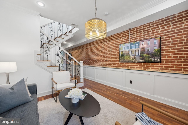 living room with crown molding, a notable chandelier, hardwood / wood-style flooring, and brick wall